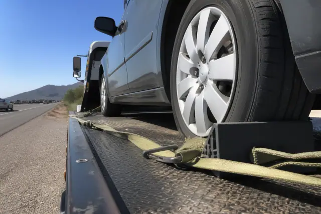 Close-up of a wheel chock securing a sedan tire on a flatbed truck on a roadside in Tucson, AZ.