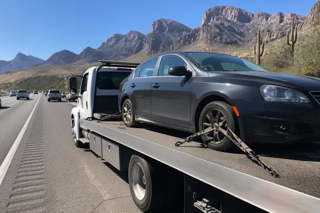 Flatbed tow truck carrying a disabled sedan on a roadside in Oro Valley, AZ with a desert mountain backdrop.