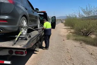 Technician checking wheel dollies on a car secured to a flatbed tow truck on a desert roadside in Tucson, AZ.