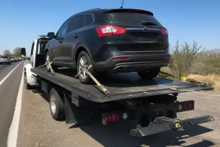 Car secured with yellow tie-down straps on a flatbed tow truck on a desert roadside in Tucson, AZ.