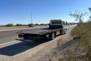Vehicle parked on a gravel highway shoulder with desert creosote bushes in Tucson, AZ.