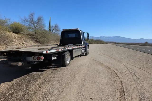 Heavy-duty truck with a flatbed transport trailer parked on a highway pull-off in Tucson, AZ.