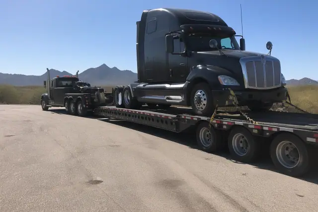 Heavy-duty truck towing a transport trailer secured with straps and chains along a desert road in Tucson, AZ.