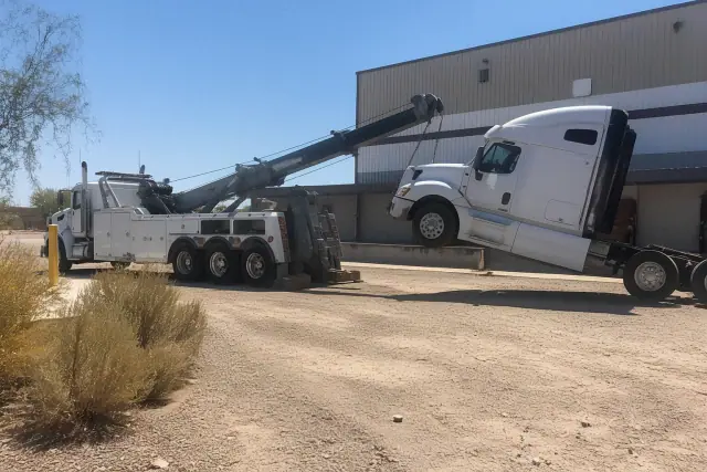 A heavy-duty wrecker truck lifting the front axle of a semi-truck at an industrial loading dock in Marana, AZ.