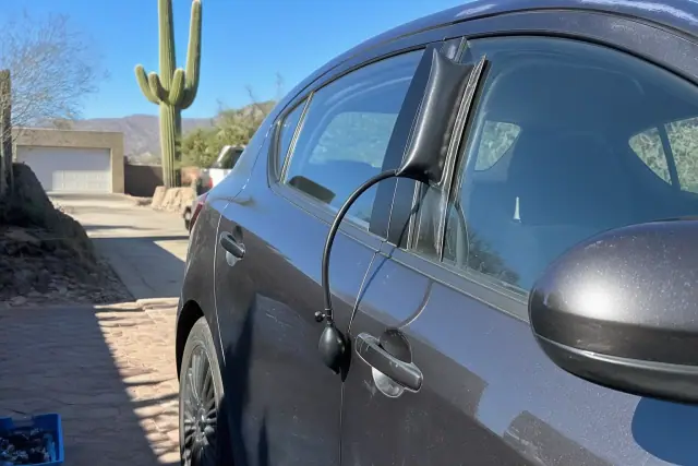 Inflatable wedge tool opening a car door in a residential driveway in Tucson, AZ, with a saguaro cactus in the background.