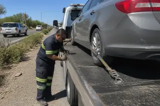 Technician checking tire straps on a vehicle secured to a flatbed tow truck on a highway shoulder in Tucson, AZ.