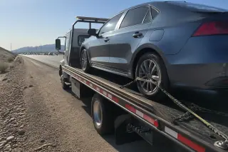Car secured with yellow straps on a flatbed tow truck on a gravel highway shoulder in Tucson, AZ.