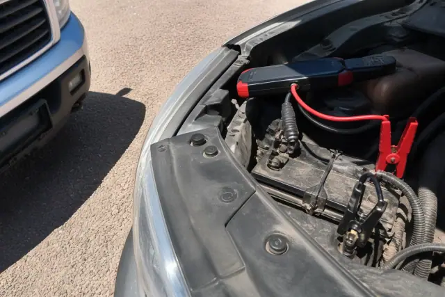 Lithium jump starter connected to a car battery on a gravel lot in Tucson, AZ.