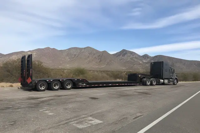 A heavy-duty truck towing a transport trailer parked by a desert road in Tucson, AZ.