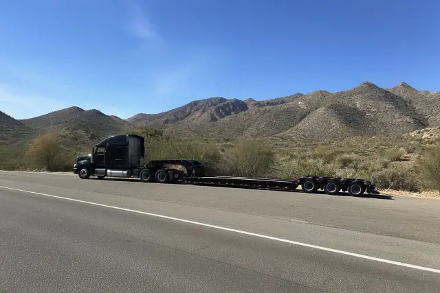 A heavy-duty truck with a transport trailer parked at a desert highway pull-off in Tucson, AZ.