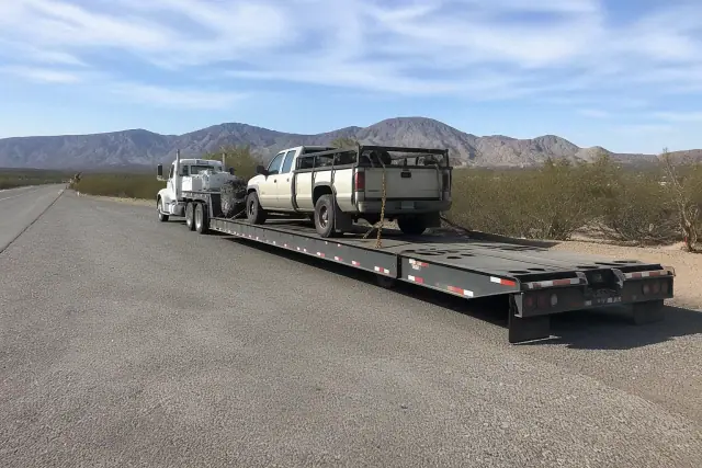 Heavy-duty tow truck with a transport trailer secured by chains parked on a roadside in Tucson, AZ.