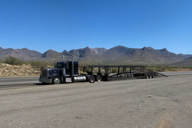 Heavy-duty tow truck with a long-distance trailer parked on a highway pull-off in Marana, AZ with desert mountains behind.