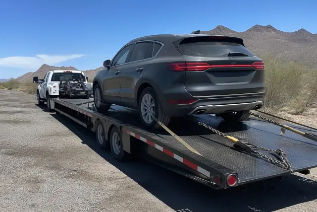 Heavy-duty truck towing a transport trailer in the Tucson, AZ desert with safety chains and tie-down ratchets secured.