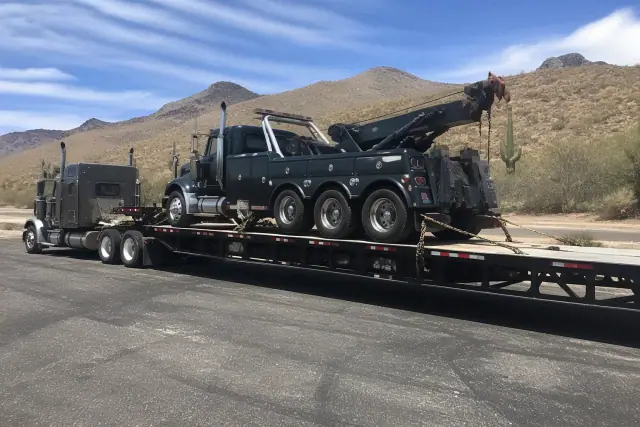 A heavy-duty truck towing a vehicle on a trailer in the desert landscape of Oro Valley, AZ.