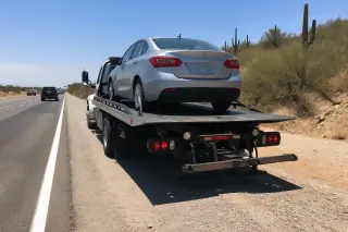 Car secured with professional tie-down straps on a flatbed tow truck on a desert highway shoulder in Tucson, AZ.