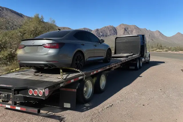 A heavy-duty truck and transport trailer parked at a desert highway pull-off in Tucson, AZ.