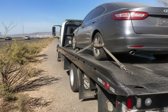 A flatbed tow truck with a secured sedan on the side of a highway in Tucson, AZ.