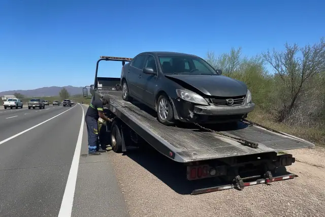 A flatbed tow truck winching a disabled sedan onto the deck on a highway shoulder in Tanque Verde, AZ.