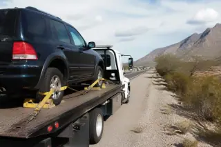 Rear wheel chocks and tensioned yellow straps securing a vehicle on a flatbed tow truck in Tucson, AZ.