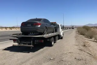 Vehicle parked on a flatbed tow truck on a dusty highway shoulder in Tucson, AZ, with traffic blurred in the background.