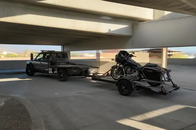 A low-clearance tow truck moving a motorcycle on a trailer in a concrete parking structure in Tucson, AZ.