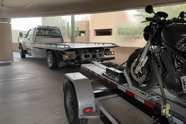 Low-clearance tow truck securing a motorcycle with nylon straps in a Tucson, AZ parking garage.