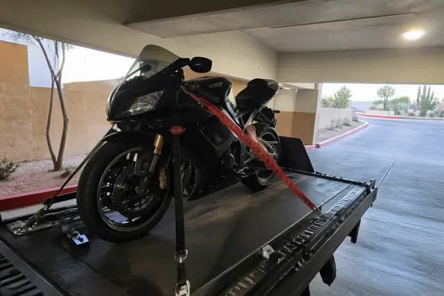 Sportbike secured with straps on a flatbed tow truck inside a concrete parking garage in Casas Adobes, AZ.