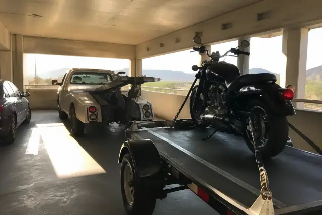 Low-clearance tow truck loading a strapped motorcycle onto a trailer in an underground parking garage in Green Valley, AZ.