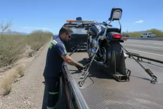 Technician checking wheel chocks on a motorcycle strapped to a flatbed truck on a gravel shoulder in Tucson, AZ.