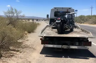 Motorcycle strapped to a flatbed tow truck on a dusty desert highway shoulder in Tucson, AZ.