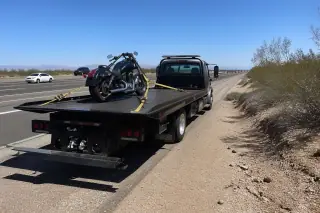 Motorcycle securely strapped to a flatbed tow truck on a gravel shoulder in Tucson, AZ.