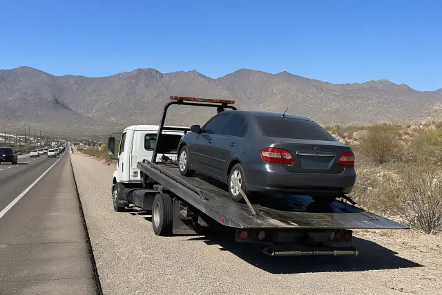 Flatbed tow truck with a disabled sedan secured on the side of a road in Marana, AZ.