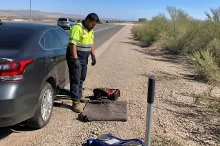 Technician clearing roadside debris near a car on a gravel shoulder in Tucson, AZ, with creosote bushes in the background.