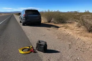 Yellow jumper cables and a portable battery pack on the ground by a towed vehicle in the Tucson, AZ desert.
