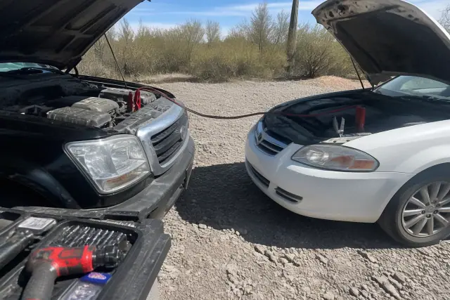Jumper cables connected to a car battery for an engine jump start service in a desert gravel lot in Tucson, AZ.