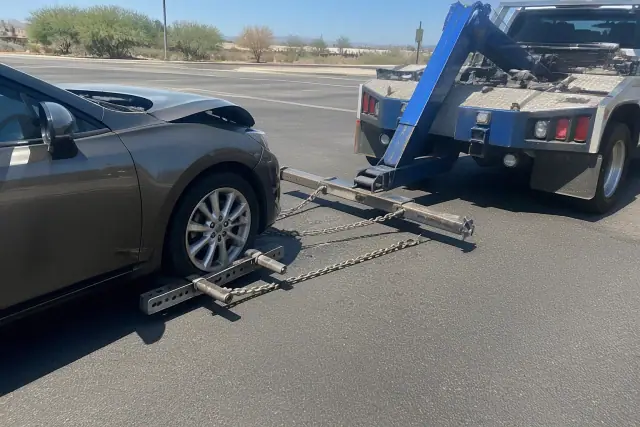 Wheel-lift recovery truck hooking up a vehicle at a sunlit asphalt intersection in Tucson, AZ.