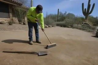 Worker sweeping residual thorns and plant fibers from leveled sandy ground at a cactus removal site in Tucson, AZ.