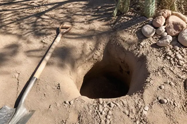 Freshly dug circular planting hole with a shovel and desert soil at a jobsite in Tucson, AZ.