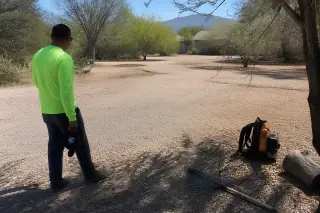 Worker using a rake to clean wood chips near desert landscaping at a job site in Tucson, AZ.